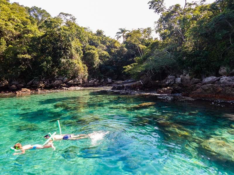 person snorkeling in blue lagoon water near jungle