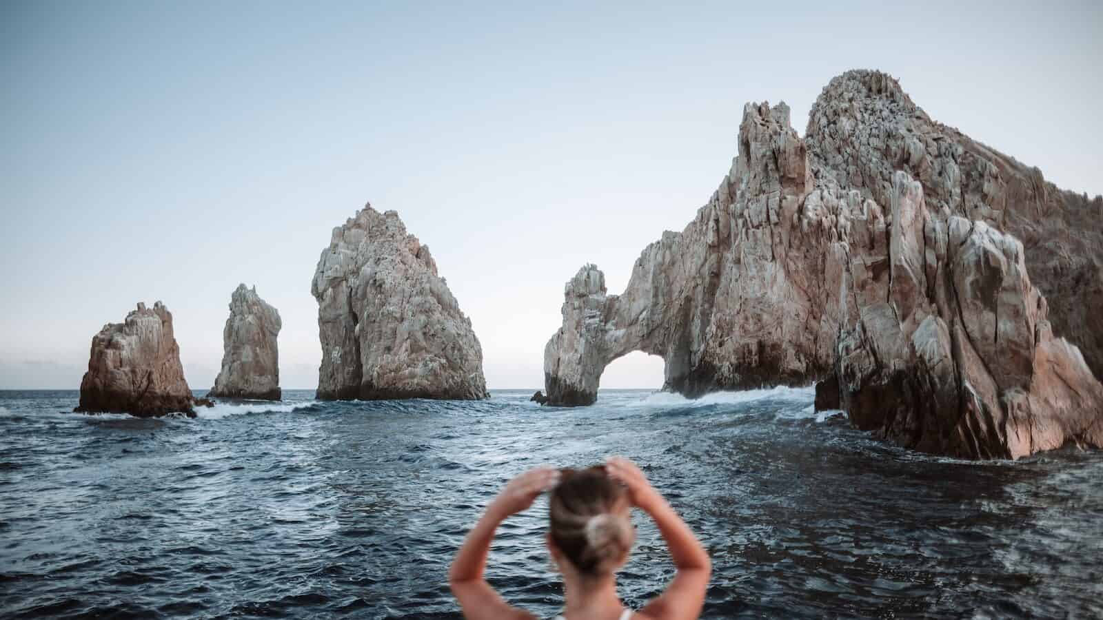 woman in white bikini on body of water near cabos rock formation during daytime
