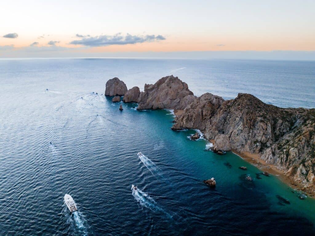 boats in dark blue ocean water by long rock formation