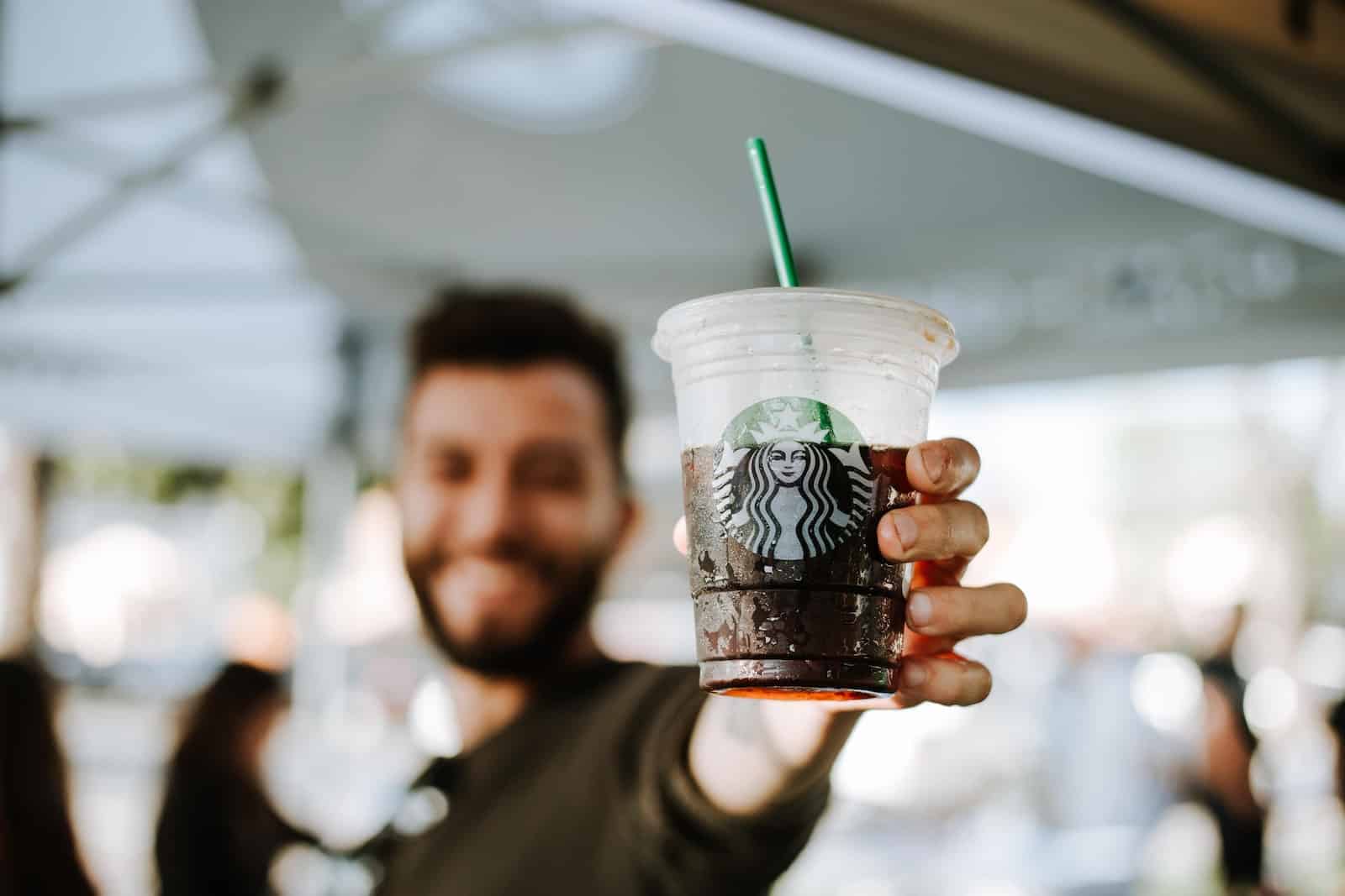 man holding Starbucks clear plastic cup with iced coffee inside