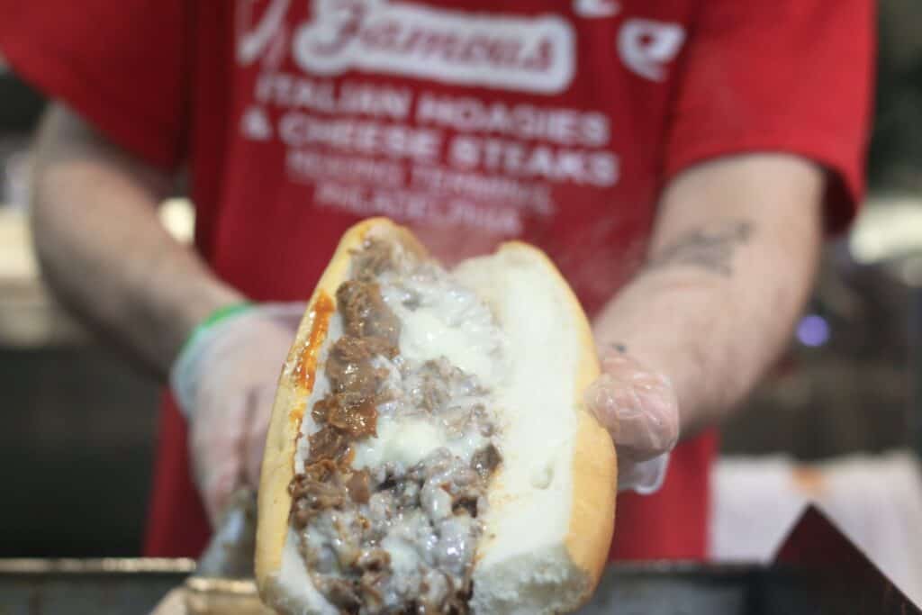 cook holding juicy cheesesteak with white melted cheese 