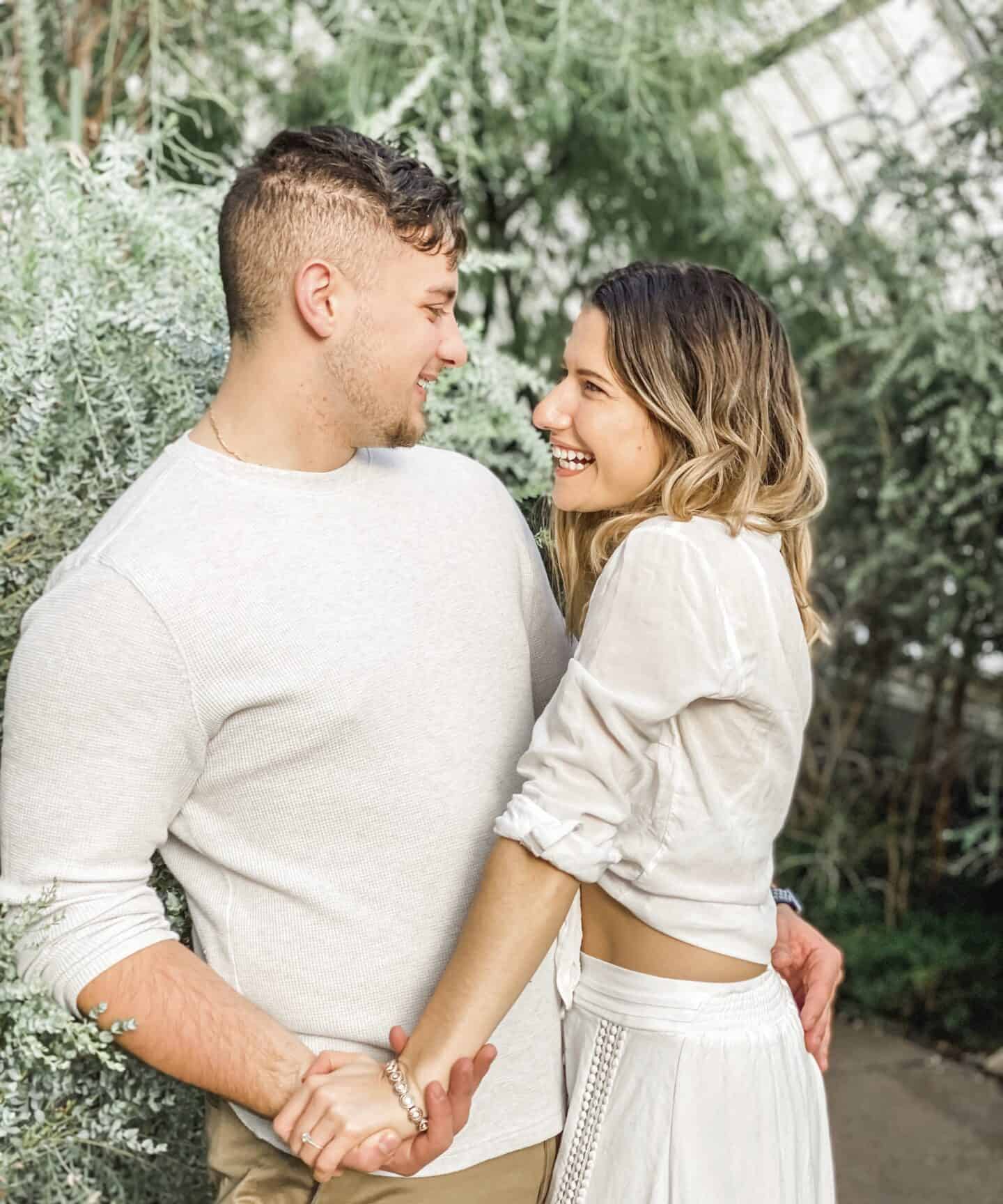adorable young engaged couple dressed in white in green garden