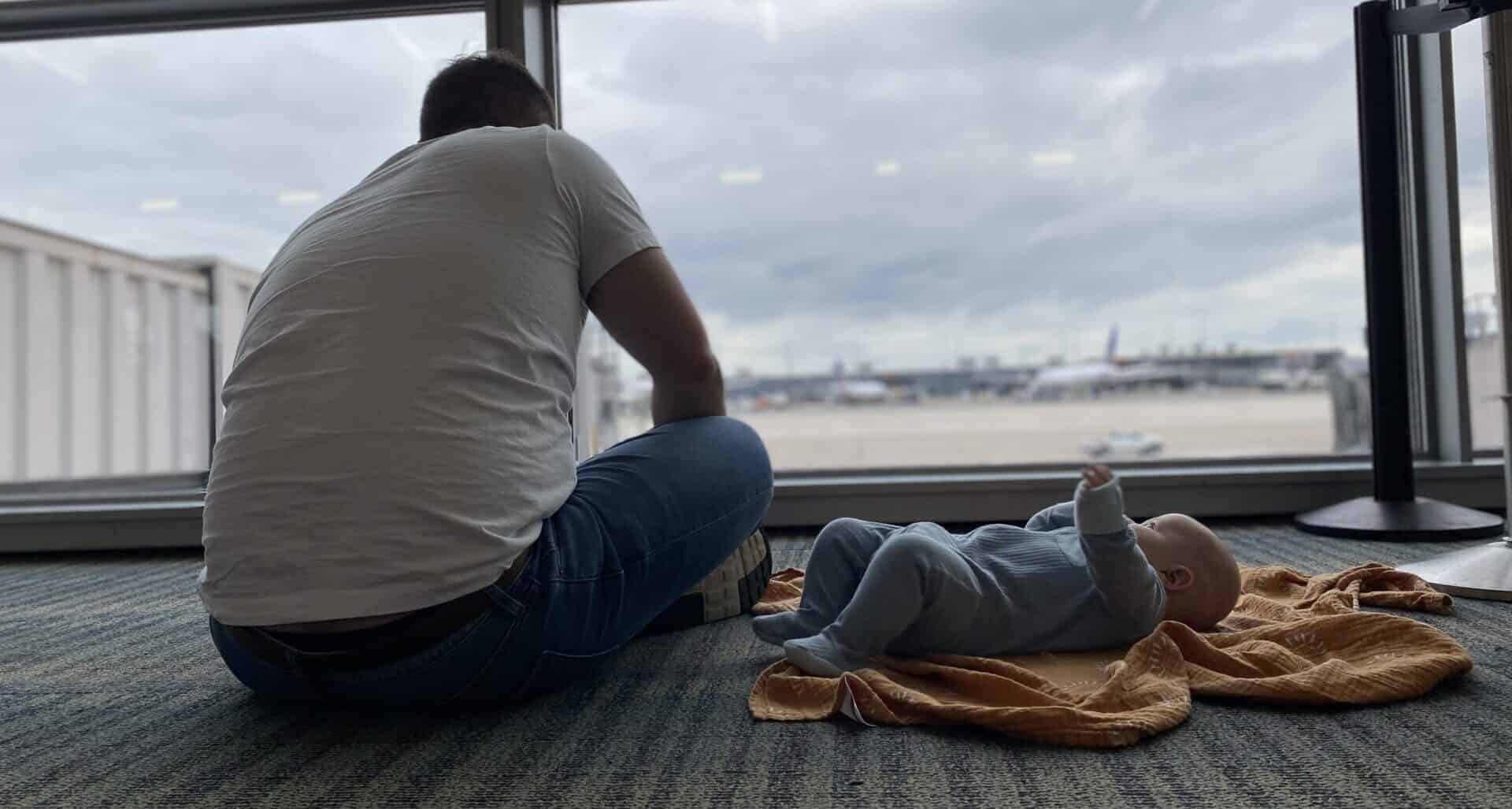 man sitting on airport floor and baby laying on airport floor