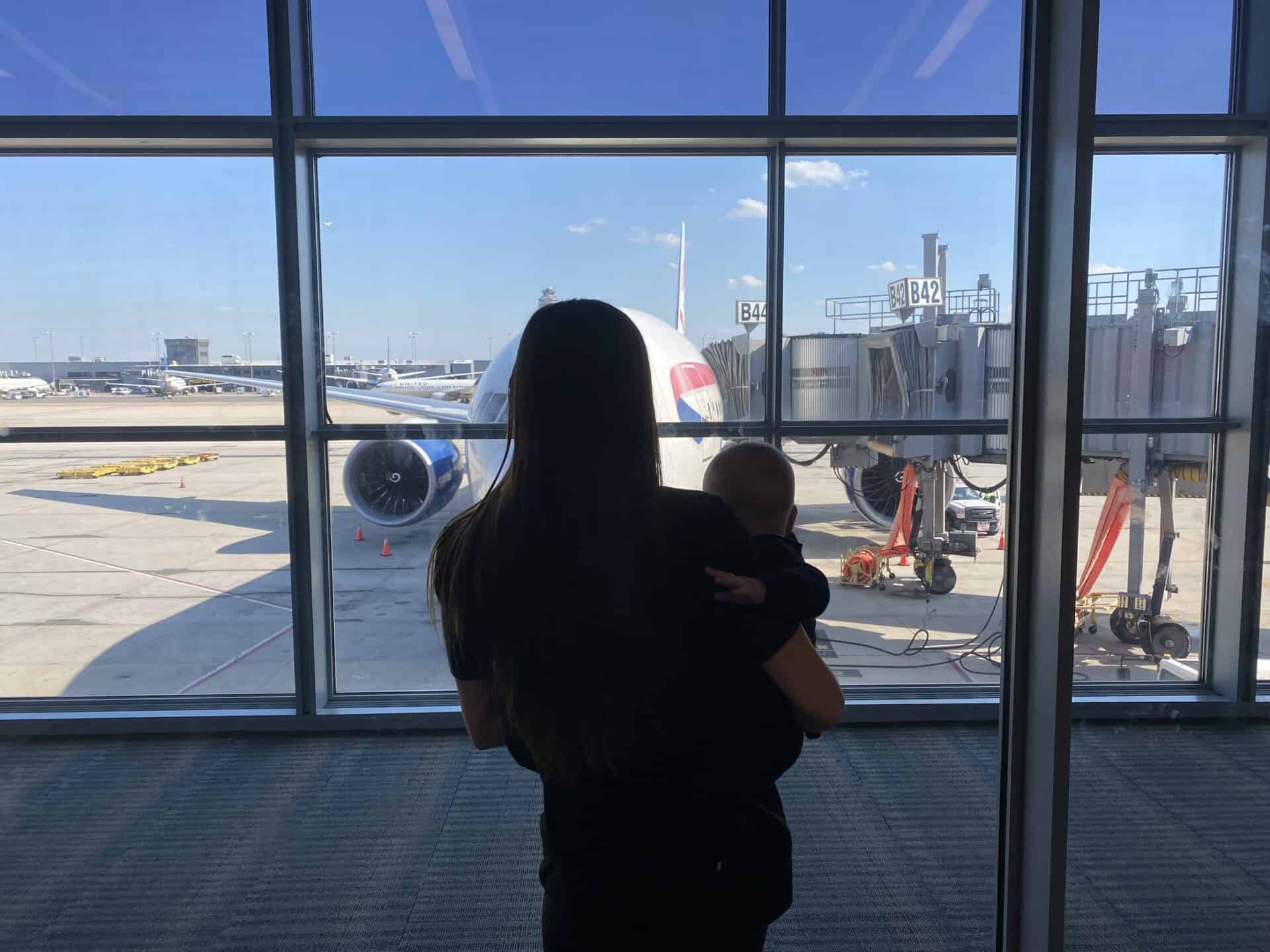 silhouette of mother and child looking at airplane through airport glass wall