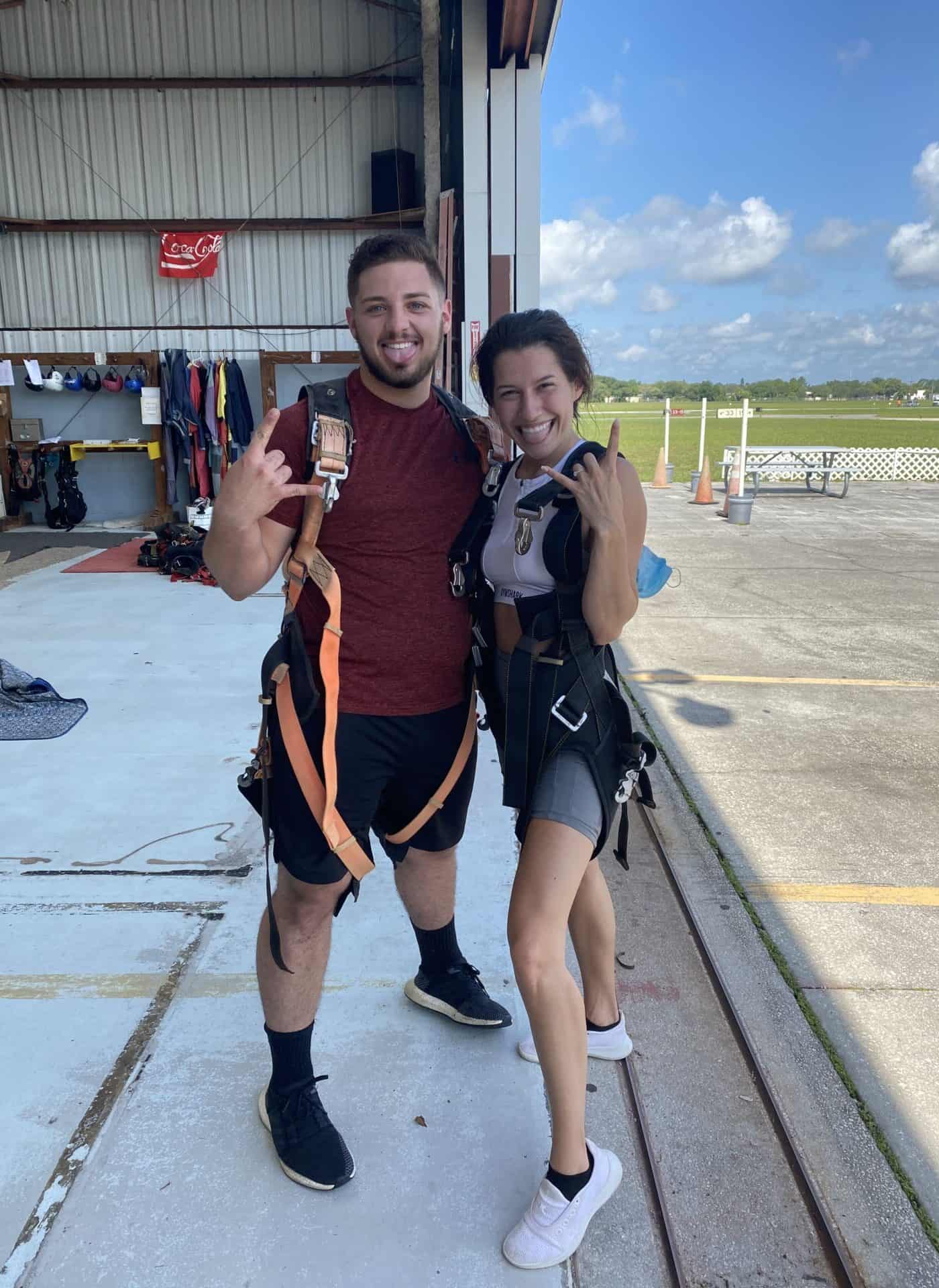 man and woman smiling in skydiving gear after jumping out of plane