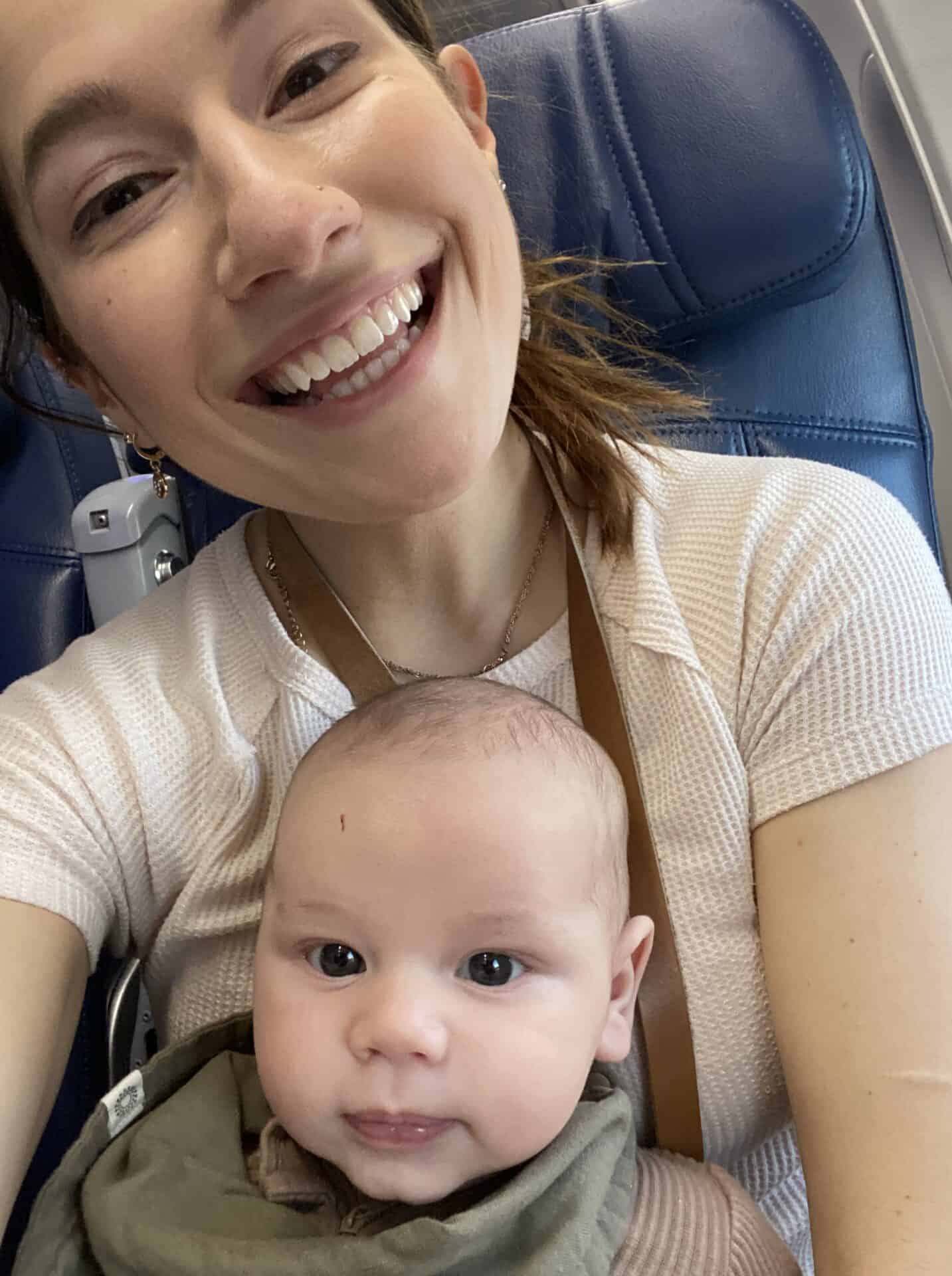 selfie of mother holding two month old baby in airplane seat