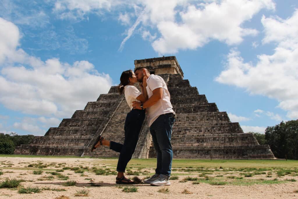 couple in blue jeans and white shirts kissing at chichenitza pyramid in mexico