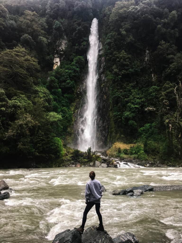 woman standing in front of epic waterfall surrounded by greenery