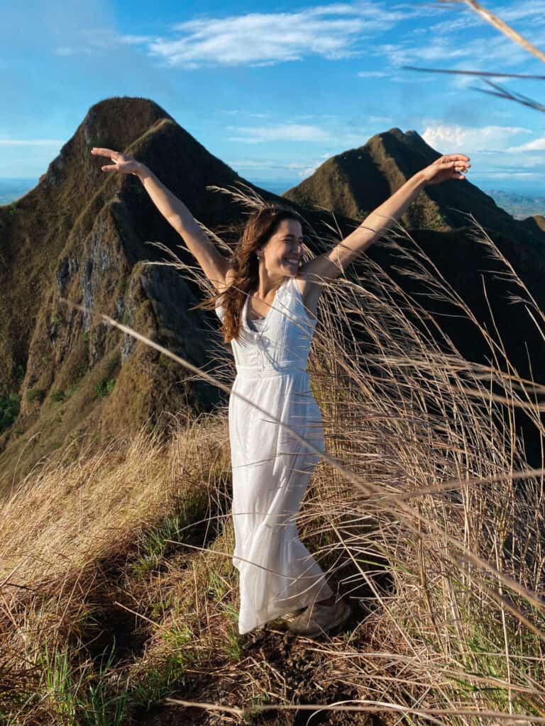 woman in white dress laughing on top of green cerro los picachos mountain range with tall yellow grass