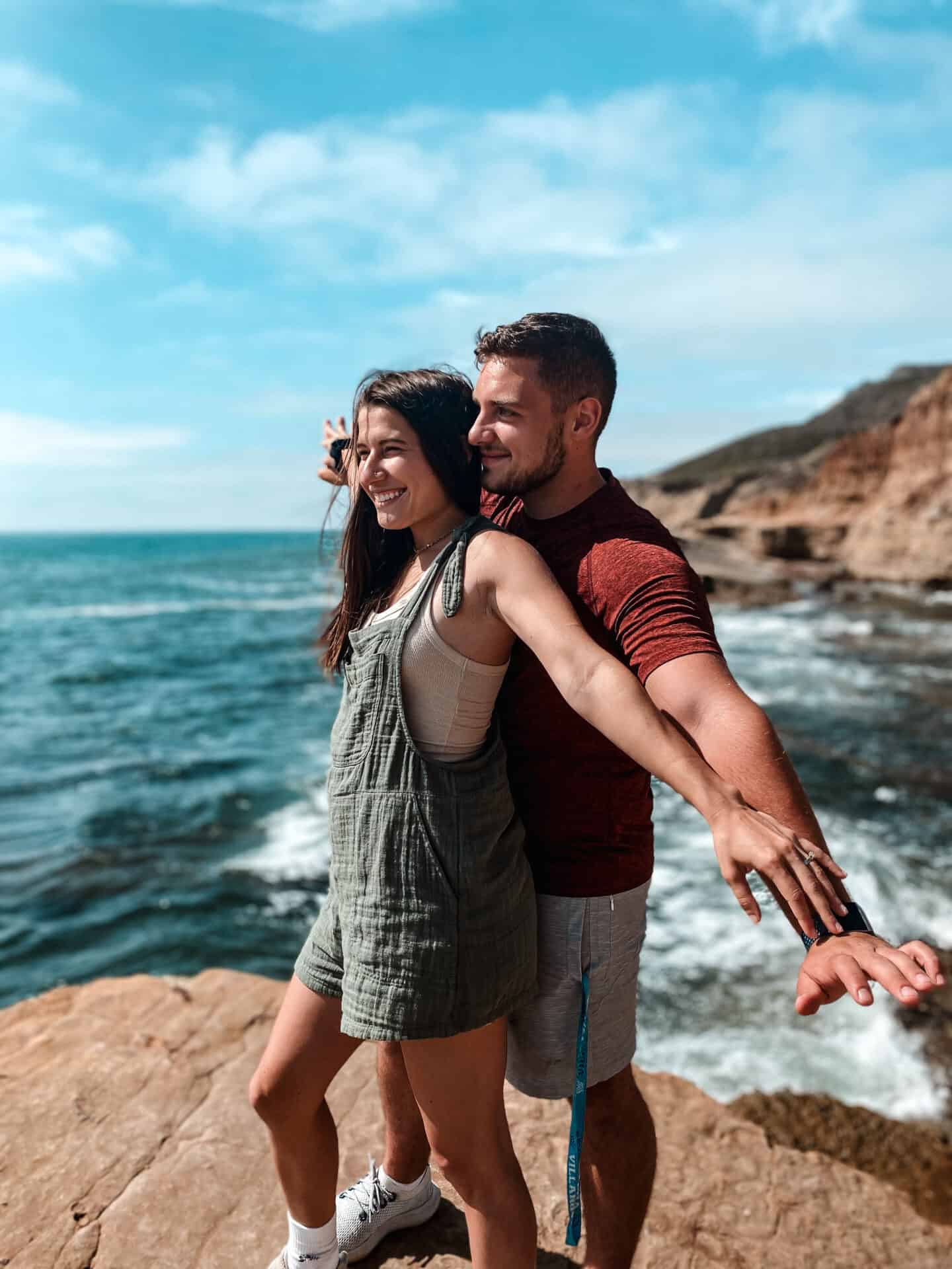 couple holding eachother like titanic on San Diego tidal pool rocks overlooking ocean with crashing waves