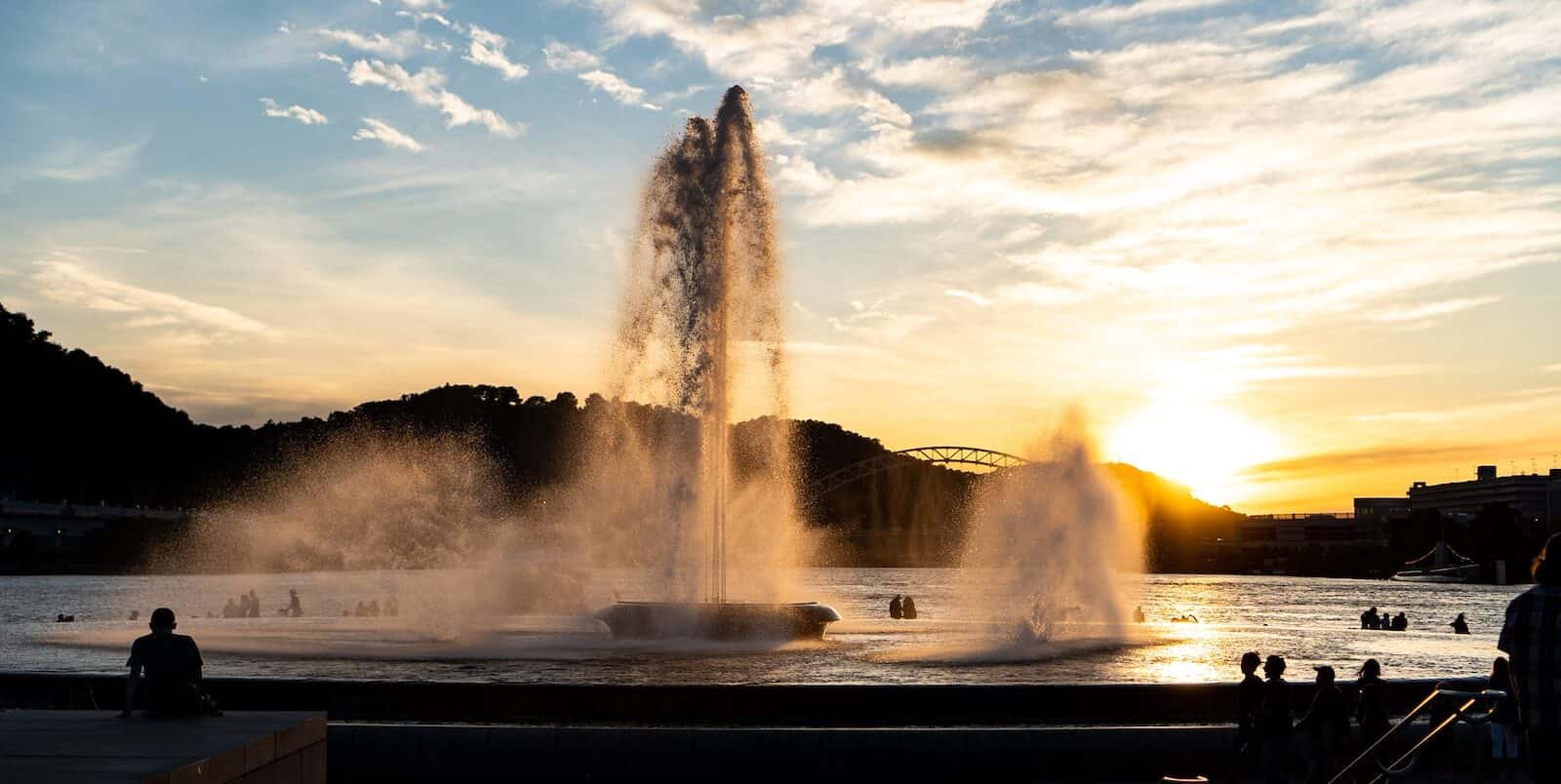 large fountain shooting water into the sky under sunset