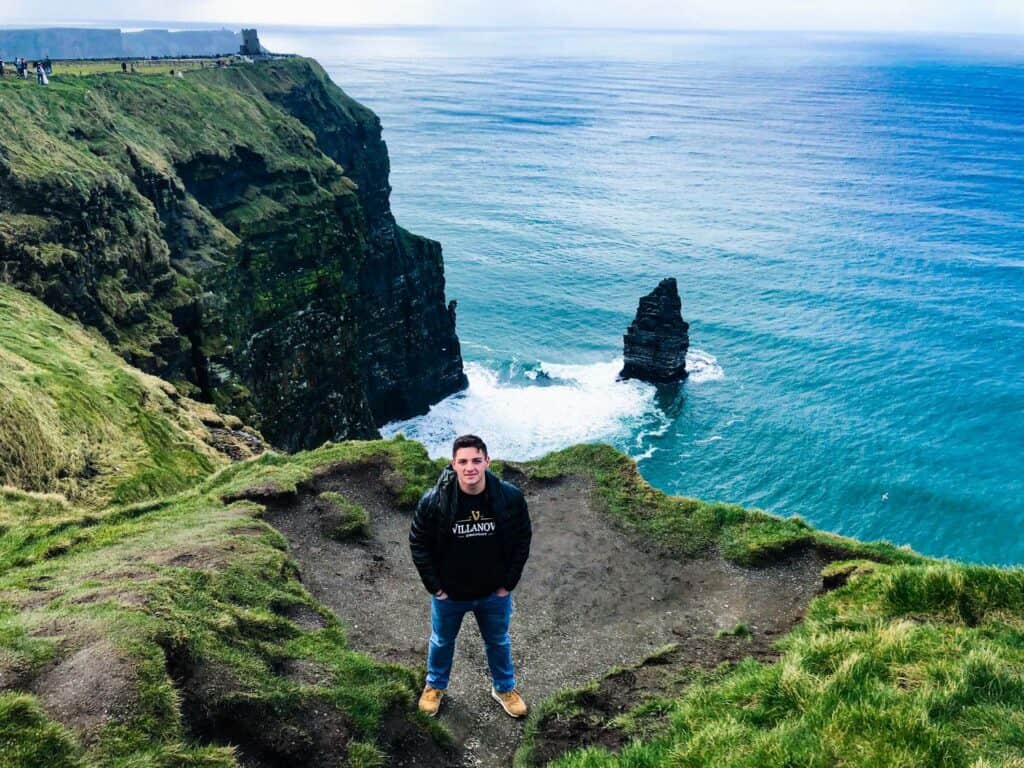 Man on grassy cliff near ocean in Ireland