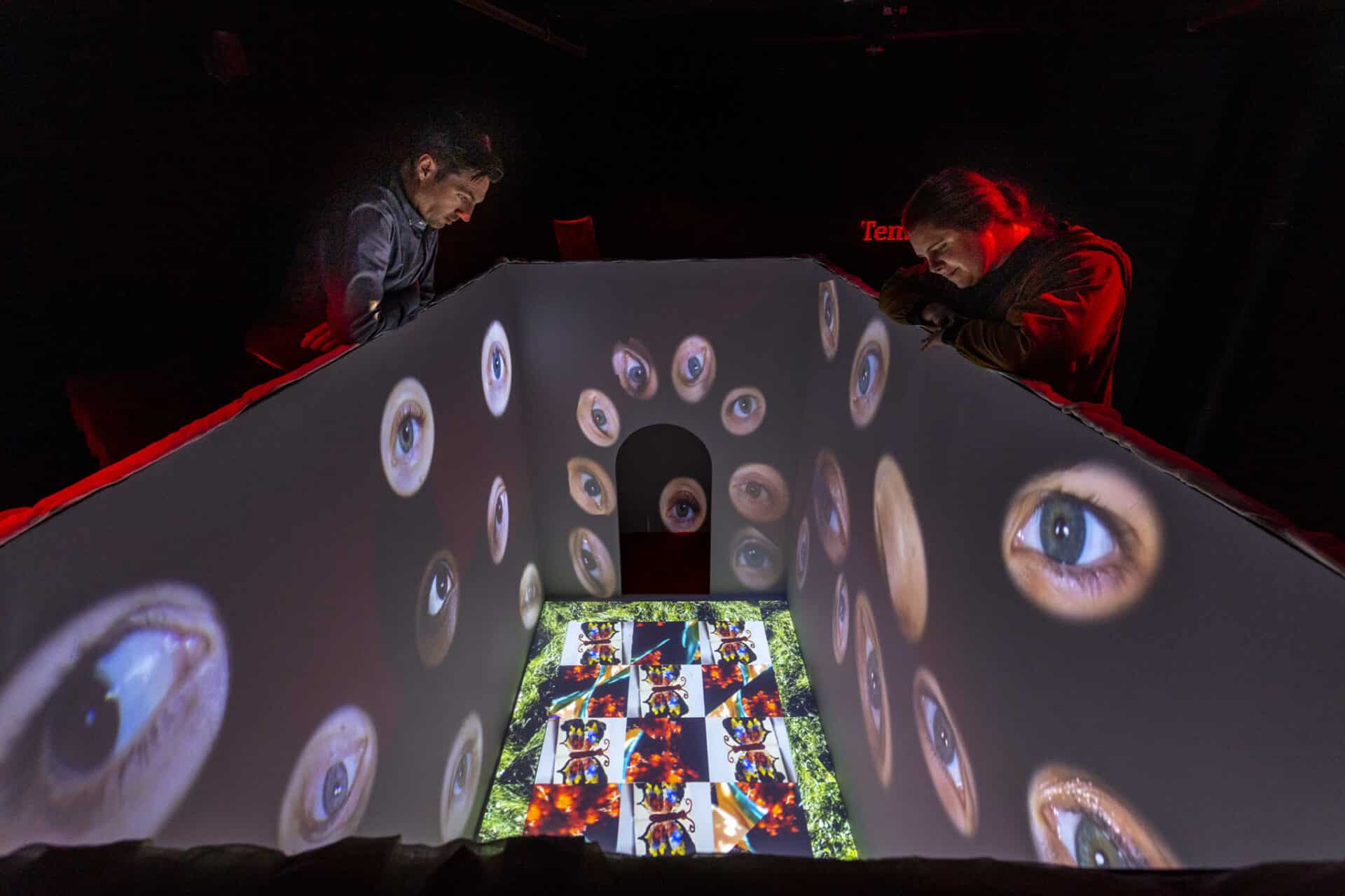 people looking at art exhibit with a screen projecting eyes