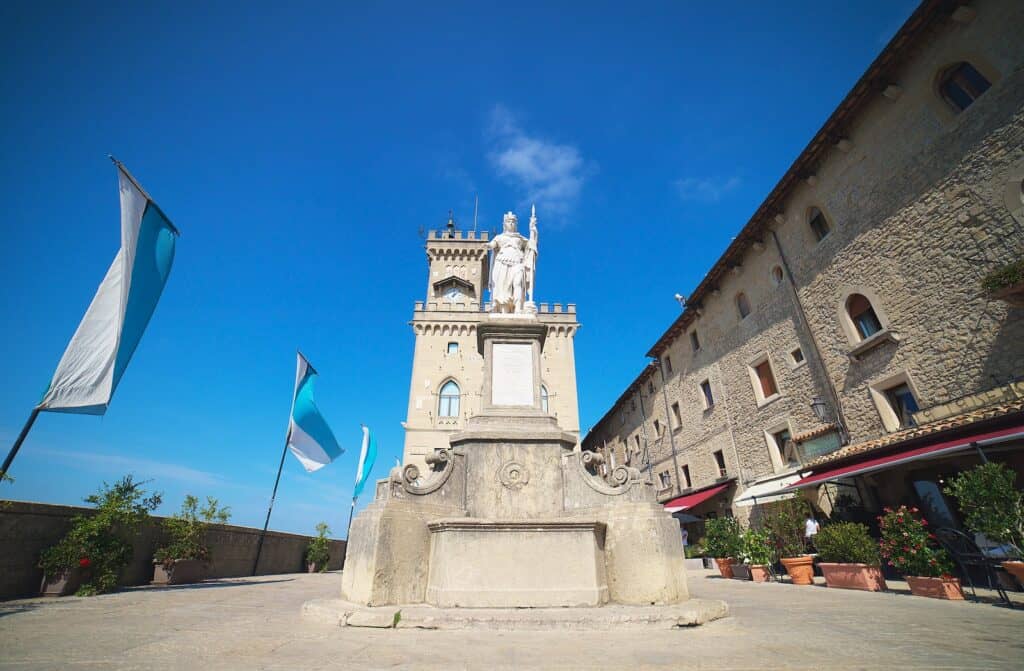 White stone statue in San Marino square with flag during daytime