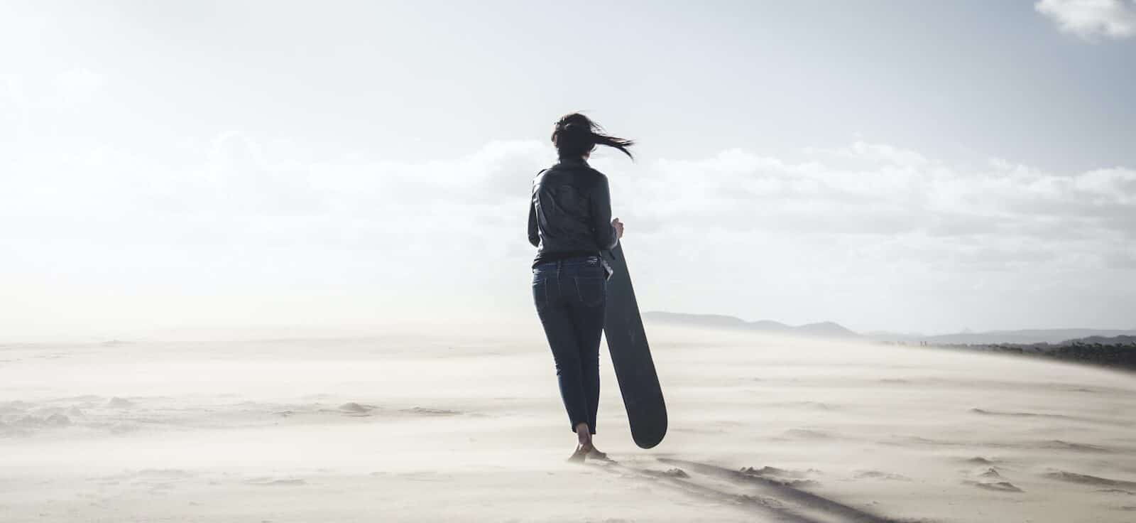 person holding snowboard in sand dunes