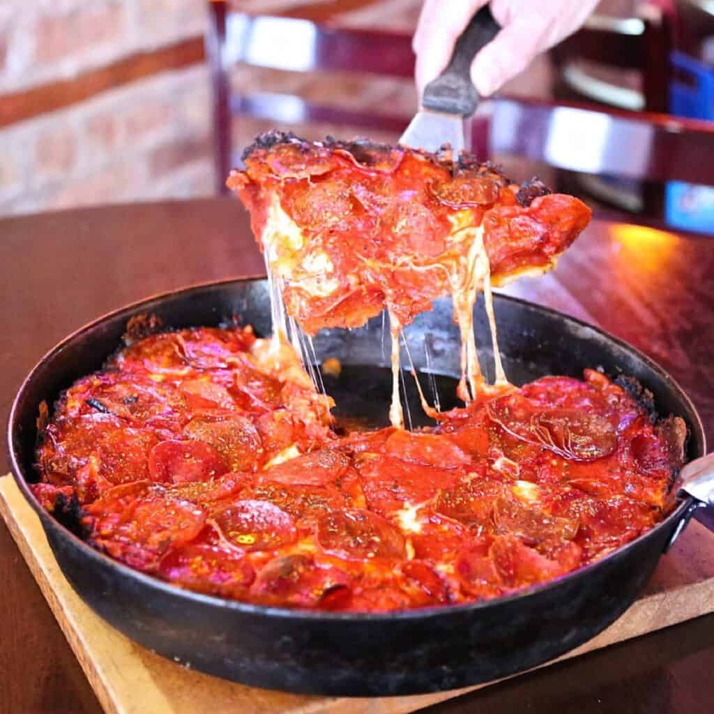 chicago style deep dish pizza with red sauce and cheesey pizza being cut