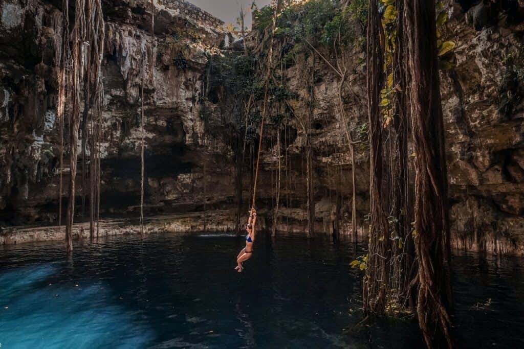 woman swinging into large dark cenote of water in the ground