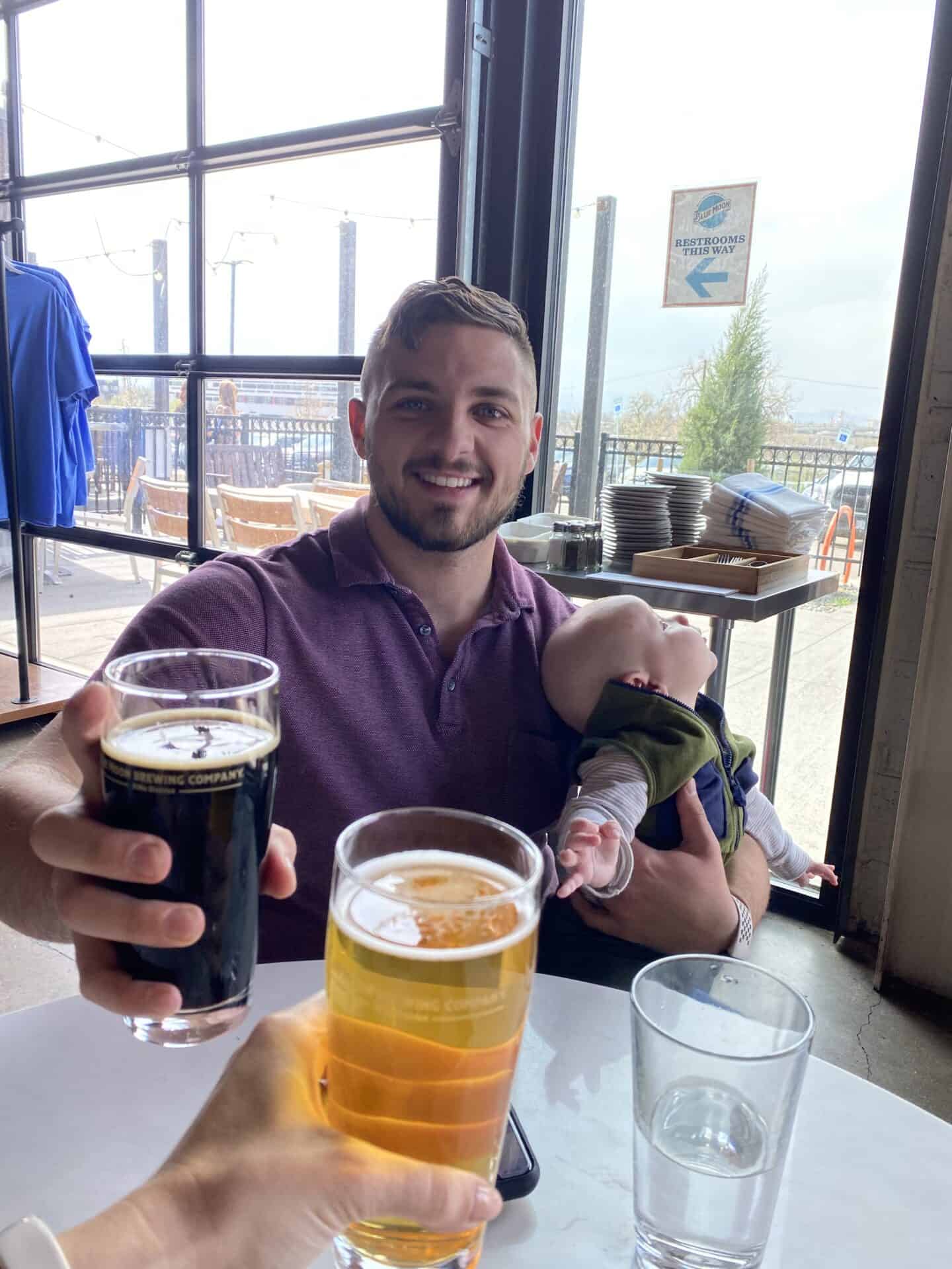 baby son sitting on fathers lap as he drinks a coors light dark beer