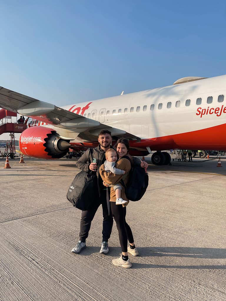 cute travel couple with baby and luggage hugging in front of an airplane