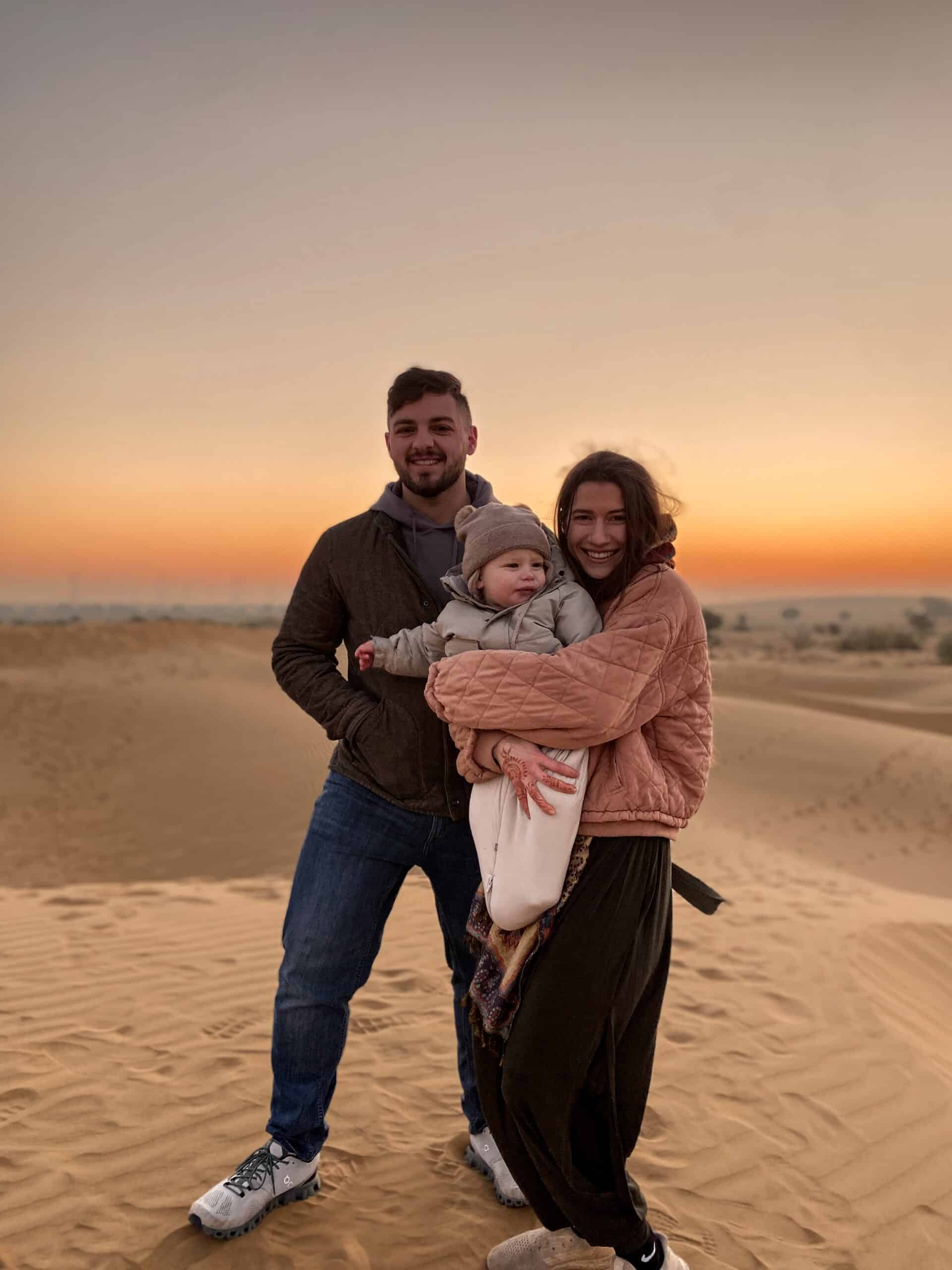 man and woman travel couple holding their toddler sun in the great indian desert during sunrise