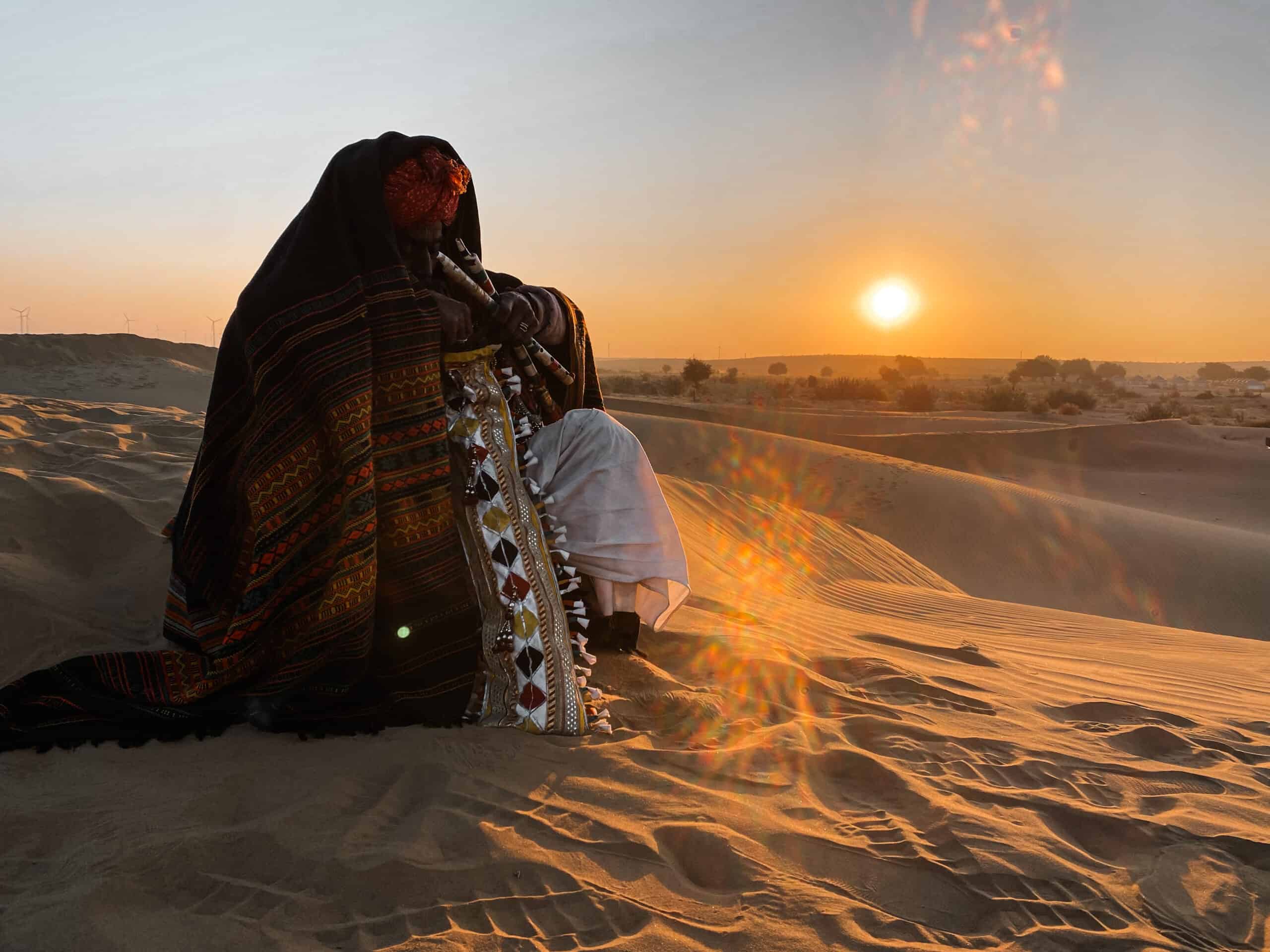 local rajasthani man covered in blankets playing a flute in the desert at sunrise