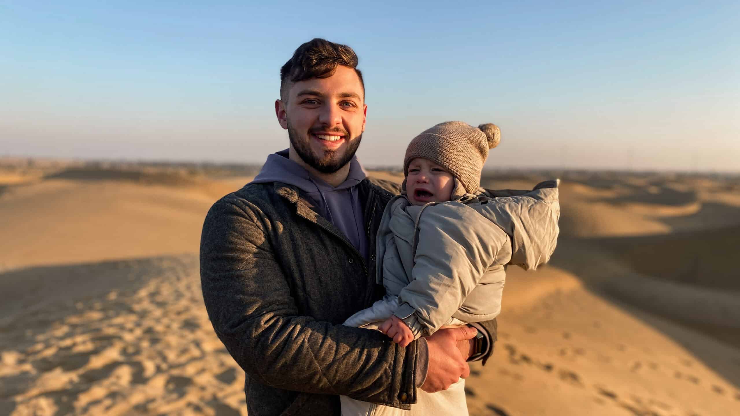 father holding son who is bundled in winter clothing in the great indian desert