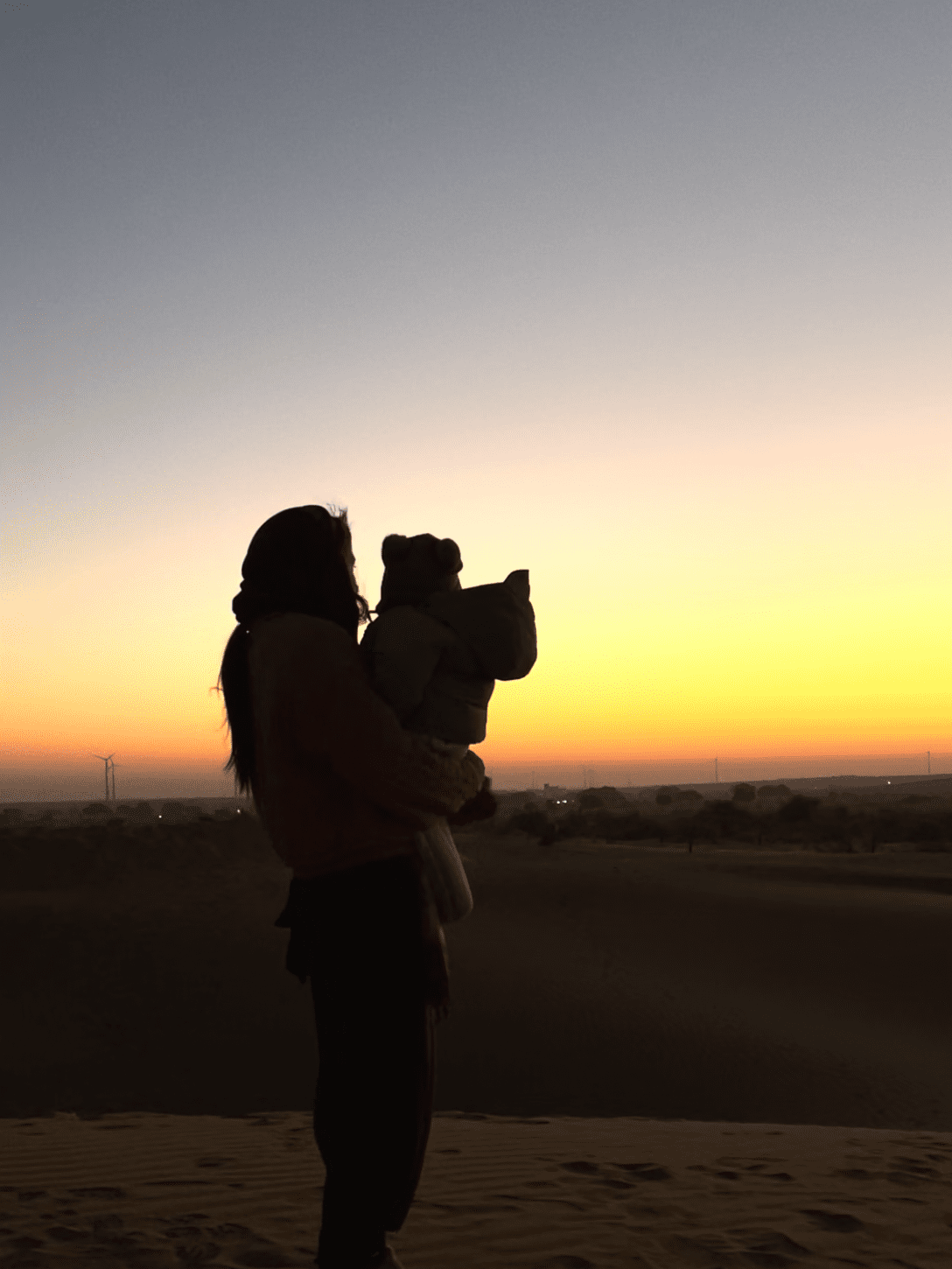 silhouette of woman holding baby overlooking desert sunrise