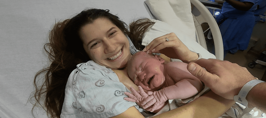 joyful mother smiling with newborn baby laying on her chest seconds after birth