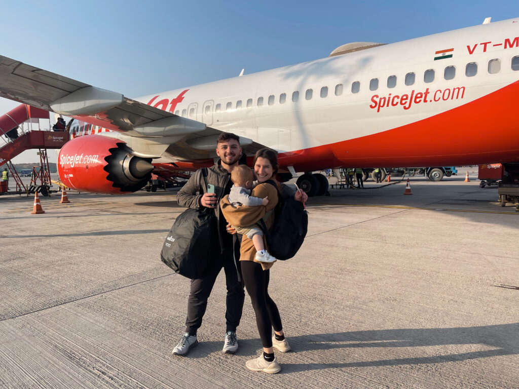 cute travel couple with baby and luggage hugging in front of an airplane