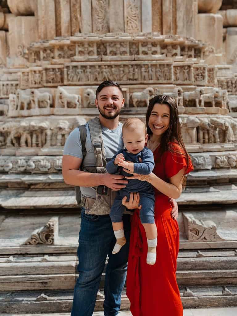 father and mother in red dress holding toddler in front of grand Jagdish Hindu Temple in Udaipur