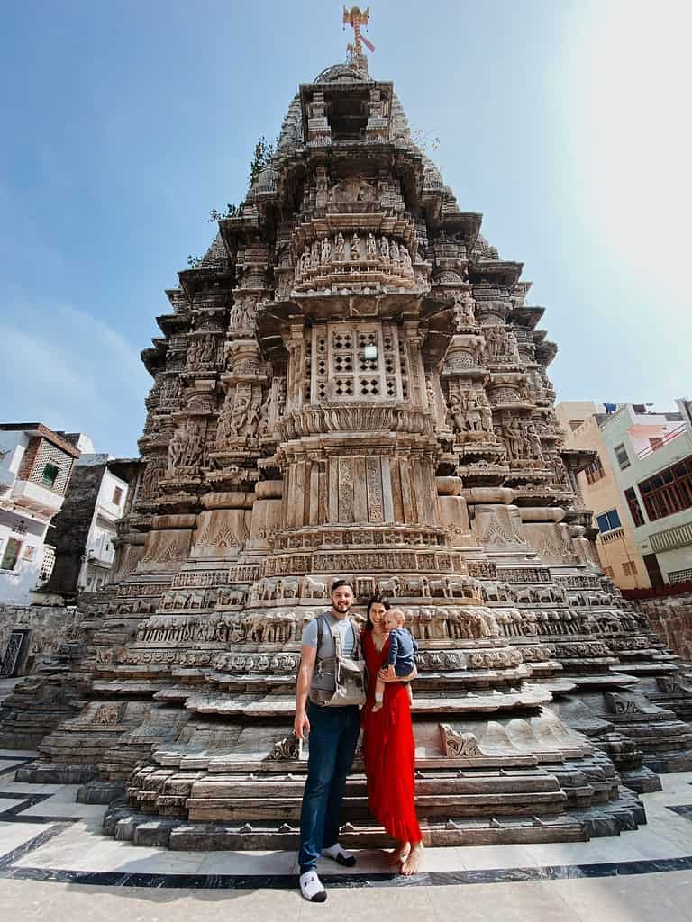 father and mother in red dress holding toddler in front of grand Jagdish Hindu Temple in Udaipur under blue sky