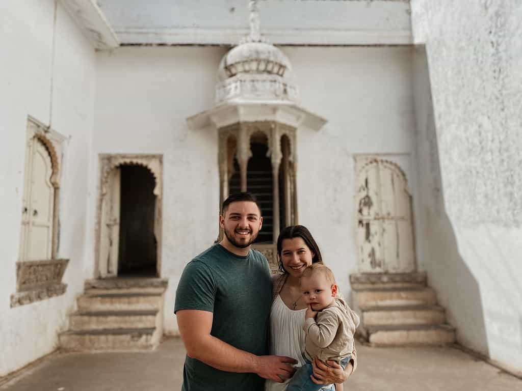 mother, father and toddler standing in the grand white monsoon palace of India