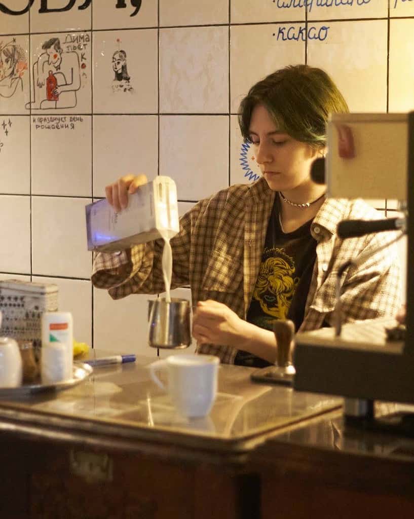hipster barista pouring milk behind coffee bar