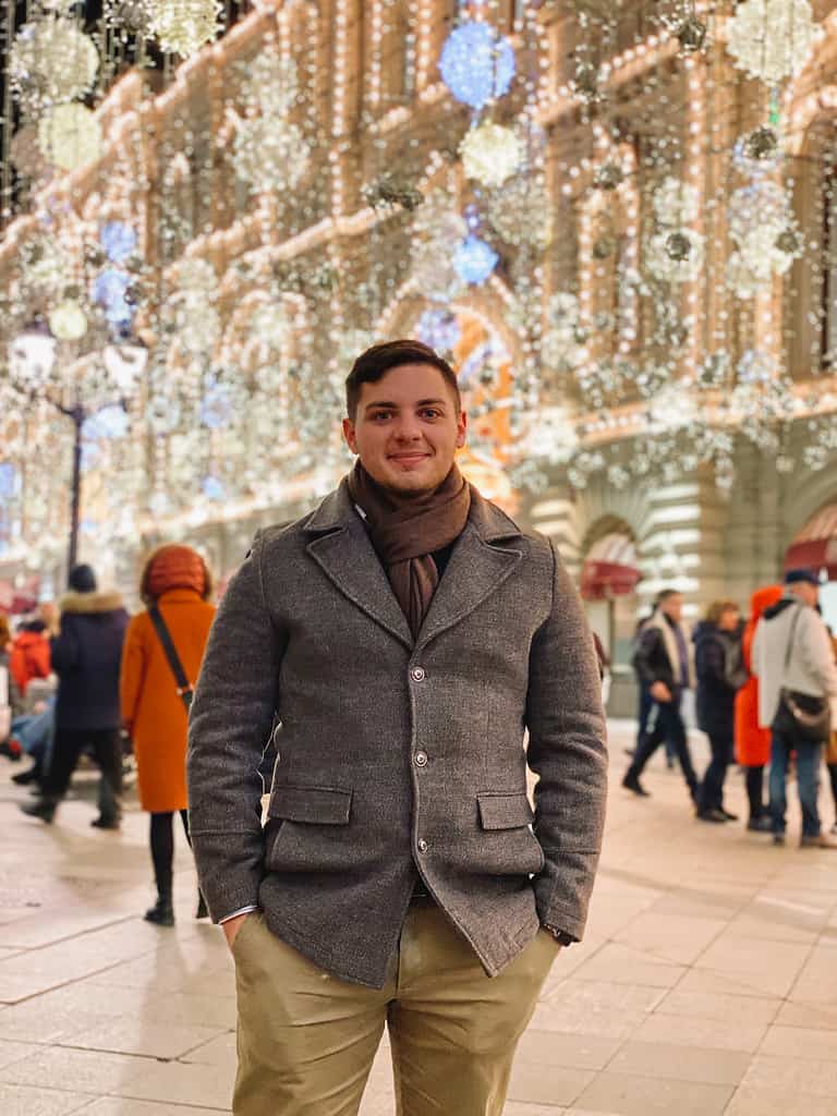 man in sinter jacket standing in arbat street moscow at night with glistening white lights strung from the buildings