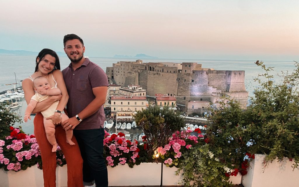 cute family with baby posing on italian roughtop overlooking castle on the sea