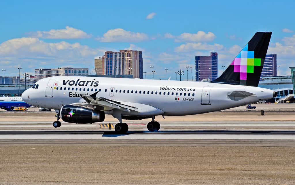 White Volaris airplane on tarmac with skyscrapers in background