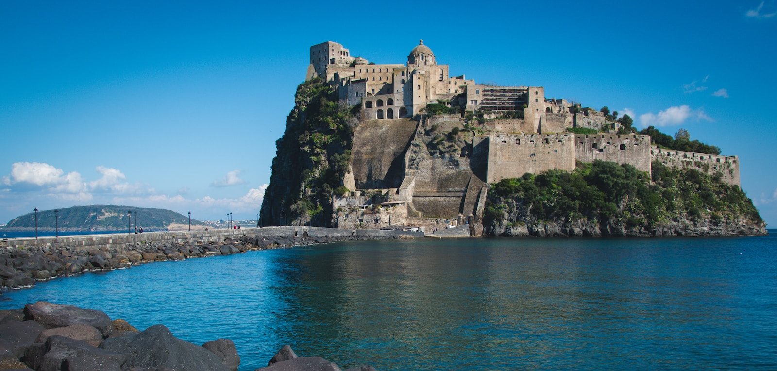 a large Italian castle sitting on top of a mountain next to a body of water