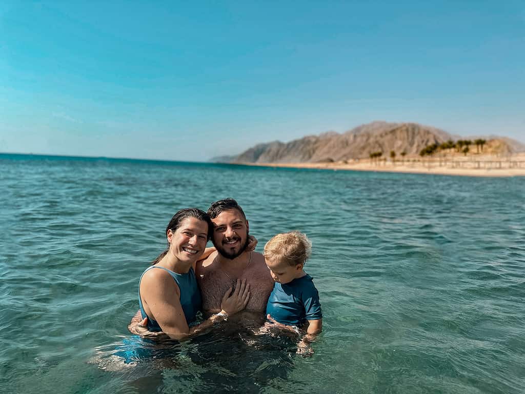 family of mother, father, and baby in a blue sea with mountains in the bakground