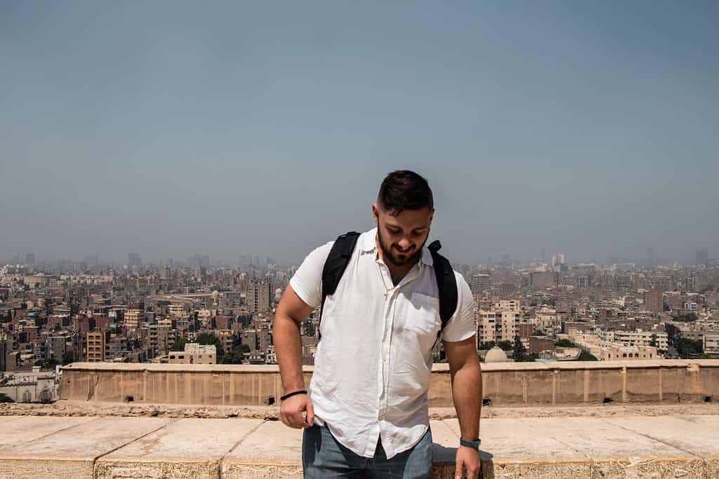 attractive young male traveler in white button down shirt standing in front of Egyptian skyline at daytime