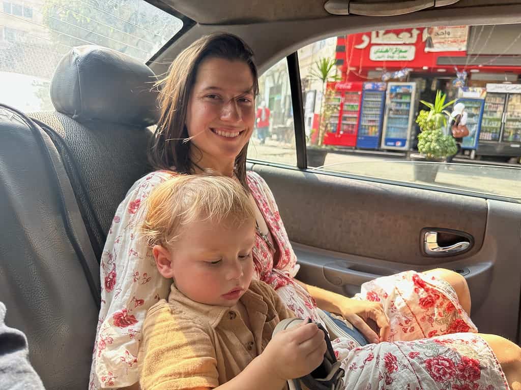 mother in white and floral dress sitting in the back of an uber with her toddler son