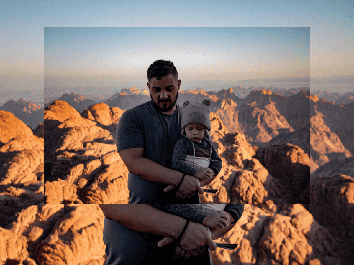 father holding toddler son in winter hat with Sinai rock mountain range in the background